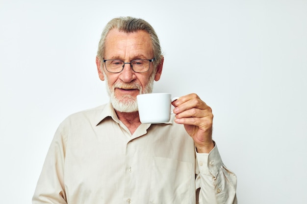 Ein älterer Mann, der einen Becher auf einem weißen Hintergrund hält und lächelt