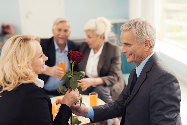 Ein älterer Mann gibt einer älteren Frau eine Rose.