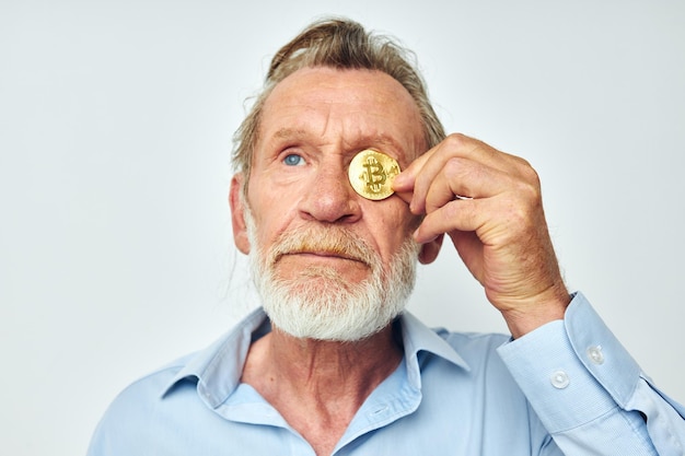 Ein älterer Mann in einem blauen Hemd bedeckt die Augen einer Bitcoin-Münze