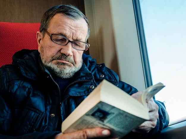 Ein älterer Mann liest ein Buch, während er im Winter mit dem Zug fährt