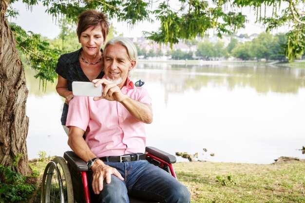 Foto ein älterer mann macht ein selfie mit seiner frau, während er im rollstuhl am see im park sitzt