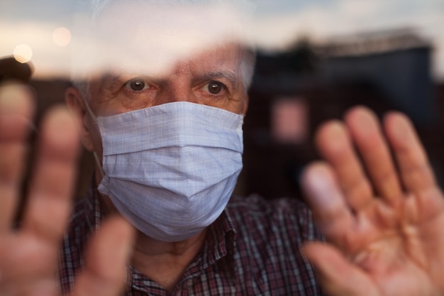 Foto ein älterer mann mit maske steht zu hause am fenster