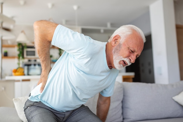 Ein älterer Mann mit Rückenschmerzen berührt seinen Rücken und veranschaulicht Ischias und einen sitzenden Lebensstil. In diesem Stockbild wird die Gesundheit der Wirbelsäule und die Bedeutung von Gesundheitsversorgung und Versicherung betont