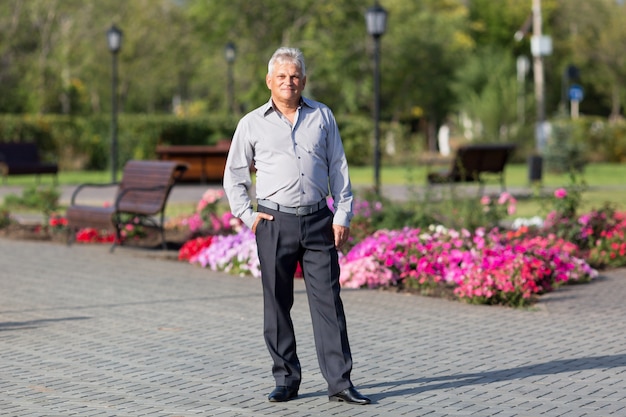 Ein älterer Mann mit weißen grauen Haaren steht in einem Stadtsommerpark