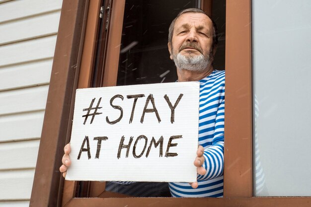 Foto ein älterer mann zeigt ein stay-at-home-poster von einem coronavirus-quarantänefenster