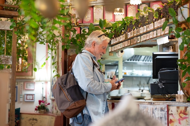 Ein älterer weißhaariger Mann bezahlt an der Kasse des Cafés mit der Anwendung auf seinem Mobiltelefon