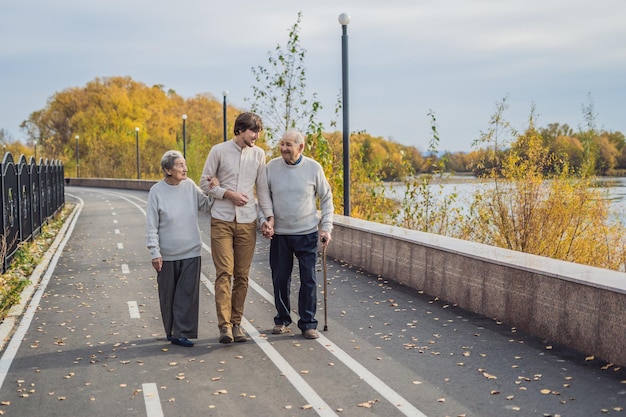 Ein älteres Ehepaar geht mit einem männlichen Assistenten oder einem erwachsenen Enkel im Park spazieren
