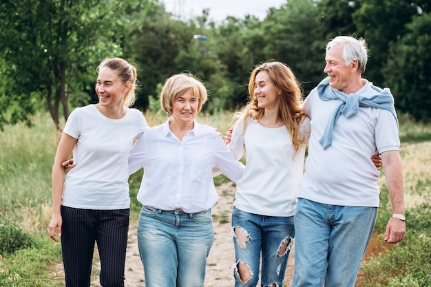 Ein älteres Ehepaar geht mit erwachsenen Töchtern in der Natur spazieren. Reifes Paar geht in den Wald. Eine Familie in weißen T-Shirts und Jeans geht im Park spazieren. Glückliche Familie. Familie kommuniziert im Freien