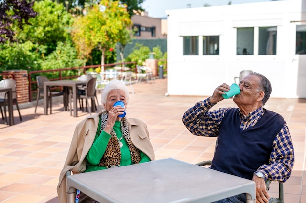 Ein älteres Ehepaar genießt einen sonnigen Tag im Garten und genießt erfrischende Getränke im Pflegeheim