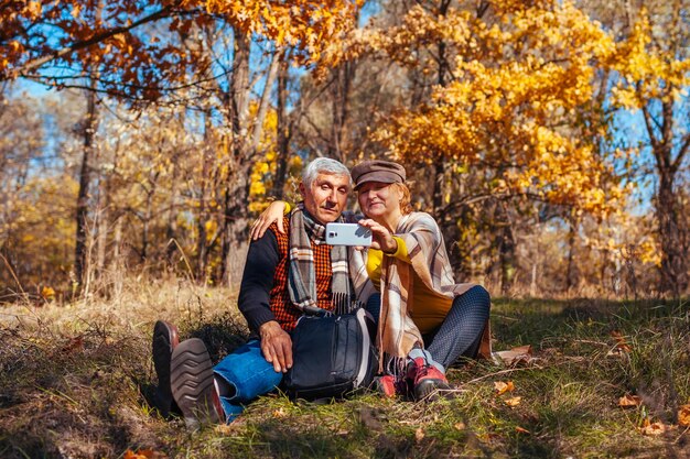 Foto ein älteres familienpaar macht ein selfie mit dem handy im herbstpark. ein pensionierter mann und eine frau genießen die natur.