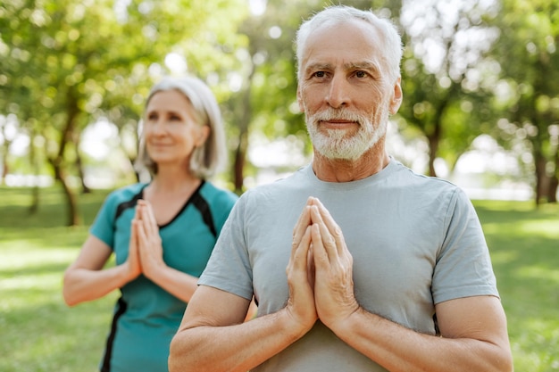 Ein älteres Paar, eine reife Frau und ein Mann, die gemeinsam im Freien im Park Yoga praktizieren