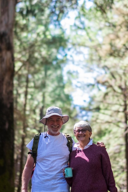 Ein älteres Paar genießt gemeinsam Freizeitaktivitäten im Freien, geht im Wald spazieren, schöne ältere Menschen lächeln und umarmen sich mit umweltfreundlichen Bäumen im Hintergrund