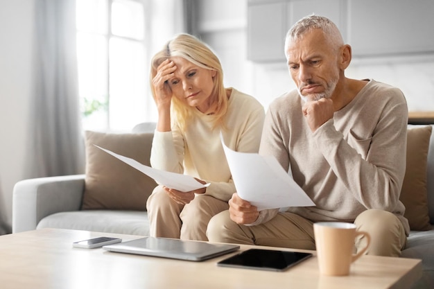 Ein älteres Paar überprüft finanzielle Dokumente, während sie zu Hause auf der Couch sitzen