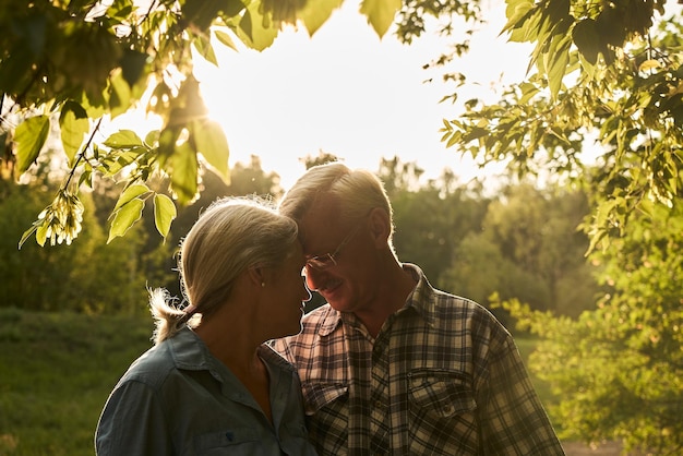 Ein älteres verliebtes Ehepaar bei einem romantischen Date in einem Sommerpark lächelt und umarmt sich vor dem Hintergrund grüner Bäume