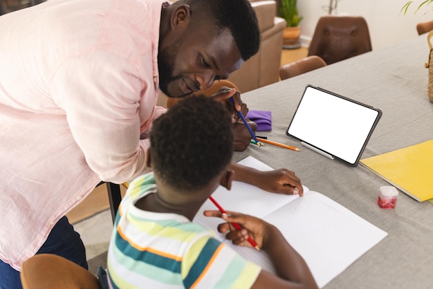 Ein afrikanisch-amerikanischer Vater hilft seinem jungen Sohn bei den Hausaufgaben an einem Tisch mit Kopierplatz