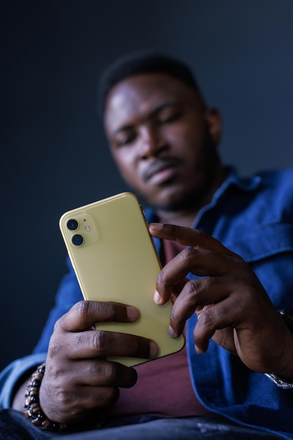 Ein afrikanischer Mann schreibt in einem Chat am Telefon, führt ein geschäftliches Gespräch, vertikales Foto