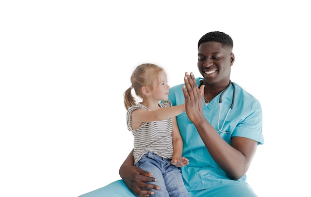 Ein afroamerikanischer Kinderarzt hält ein kleines glückliches Mädchen auf seinem Schoß, lacht und klatscht in die Hände. Familienarzt