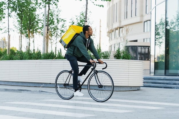 Ein afroamerikanischer Kurier mit einem gelben Rucksack auf einem Fahrrad fährt draußen