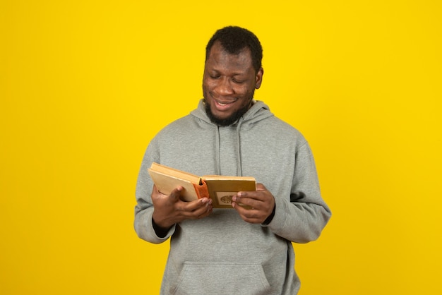 Ein afroamerikanischer lächelnder Mann, der ein Buch in der Hand liest, steht über der gelben Wand.