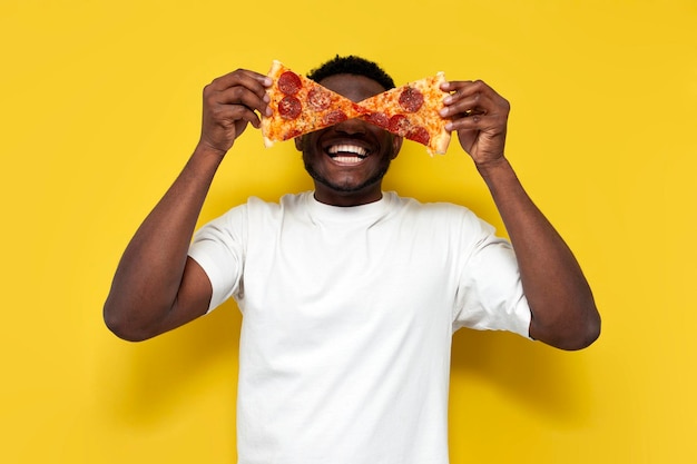 Ein afroamerikanischer Mann in weißem T-Shirt hält zwei Stücke Pizza vor seinen Augen und schreit