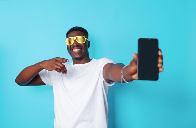 Ein afroamerikanischer Mann mit modischer Brille hält ein Mobiltelefon in seinen Händen und zeigt