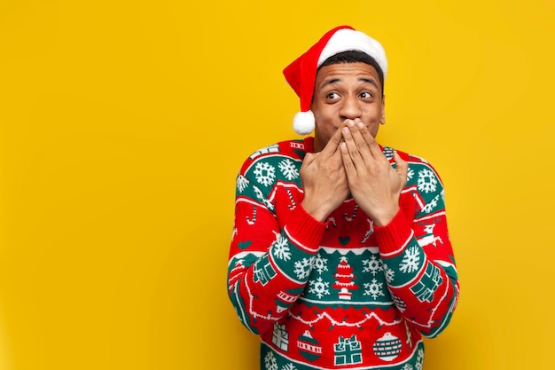 Ein afroamerikanischer Typ in Neujahrskleidung schämt sich und lacht und bedeckt seinen Mund