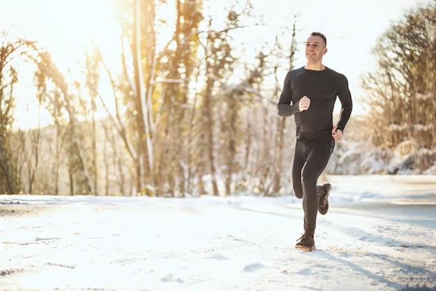 Ein aktiver junger Mann läuft während des Wintertrainings draußen auf der Forststraße.