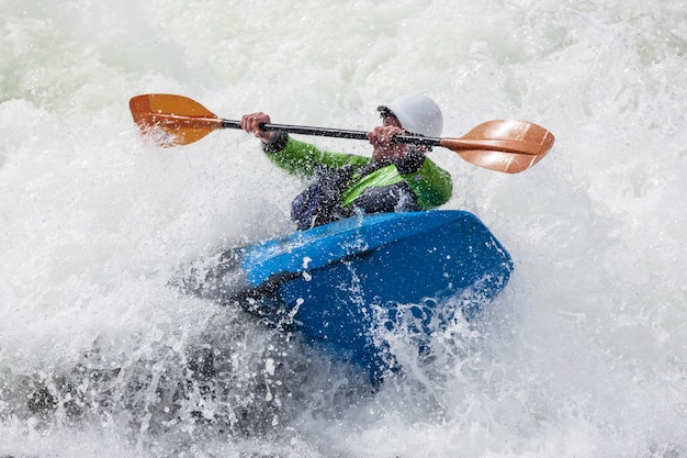 Ein aktiver männlicher Kajakfahrer, der in rauem Wasser rollt und surft