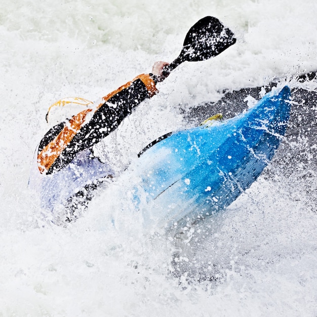 Ein aktiver männlicher Kajakfahrer, der in rauem Wasser rollt und surft