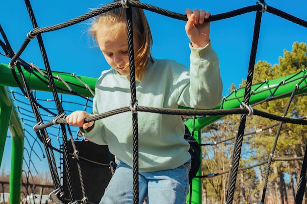 Foto ein aktives zehnjähriges mädchen kletterte auf einem spielplatz vor strahlend blauem himmel auf ein seilnetz