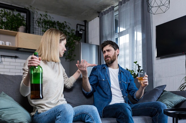 Ein alkoholkranker Ehemann streitet sich mit seiner Frau, die zu Hause auf der Couch sitzt