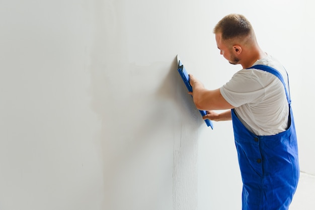 Ein allgemeiner Arbeiter in Overalls verwendet eine Kelle, um die Wand mit Zement zu bedecken