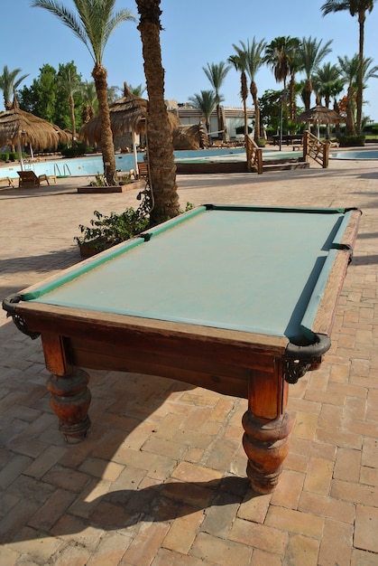 Ein alter Billardtisch steht in einem verlassenen Hotel in der Nähe des Pools und der Palme auf einem Fliesenboden