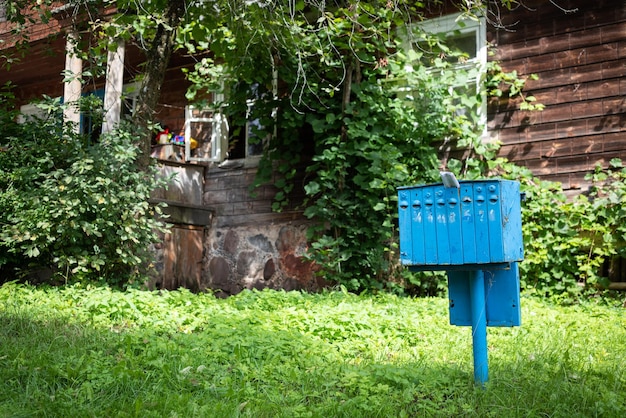 Ein alter blauer Eisenbriefkasten für Post und Korrespondenz in einem Dorf in der Nähe eines mit Grün bewachsenen Hauses