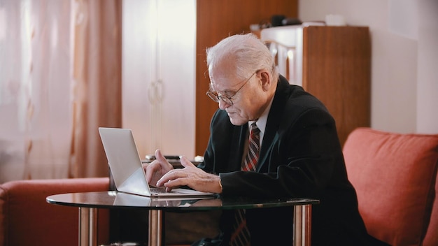 Ein alter Mann mit Brille sitzt neben dem Laptop im Zimmer