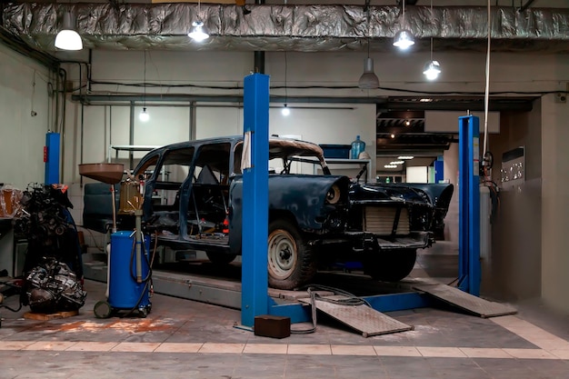 Ein altes klassisches Retro-Auto in schwarzer Farbe steht auf einer blauen Hebebühne zur Reparatur, Restaurierung und Restaurierung in einer Fahrzeugwartungs- und Tuningwerkstatt der Autoservicebranche