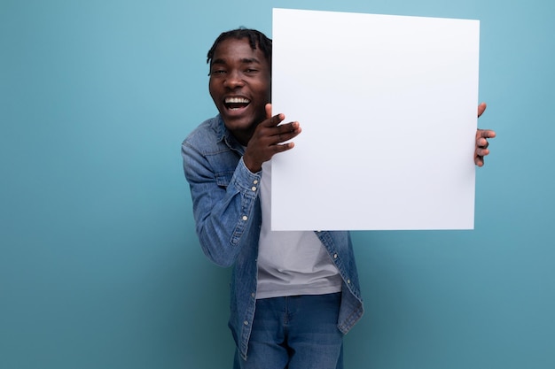 Ein amerikanischer Mann mit Dreadlocks in einer Jeansjacke führt ein Papierplakat mit einer Attrappe vor