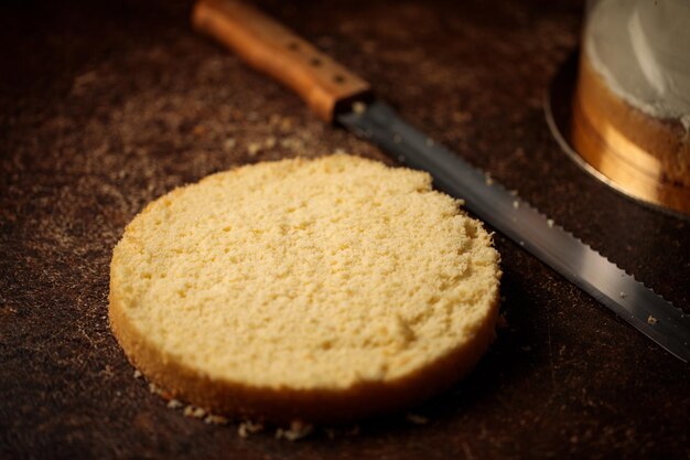 Ein angeschnittener Biskuit für einen Kuchen und ein Konditormesser auf einem Tisch in gedämpftem Licht