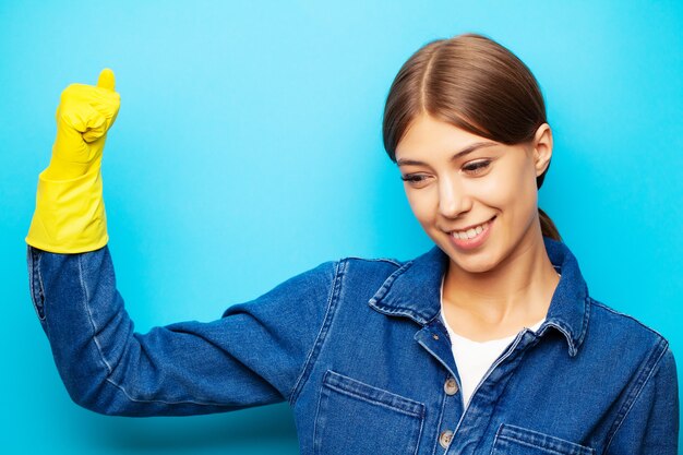 Ein Angestellter einer Reinigungsfirma in Overalls und gelben Handschuhen, die auf einem blauen Hintergrund aufwerfen