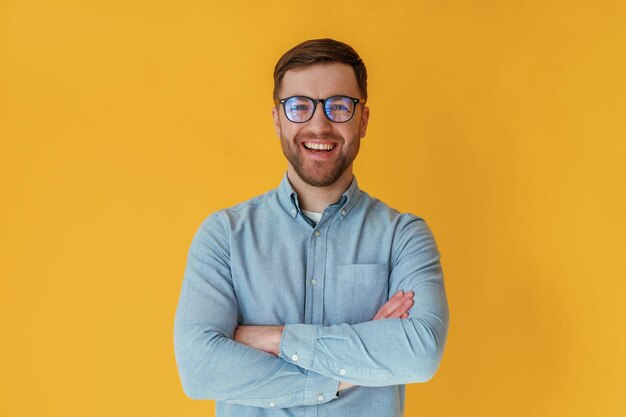 Ein ansprechender Mann in blauem Hemd steht mit gekreuzten Armen vor einem gelben Hintergrund.