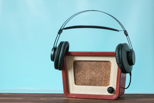 Ein antiker Radioempfänger mit schwarzen Kopfhörern auf einem Holztisch auf blauem Grund. Technik zur Ton- und Videowiedergabe.