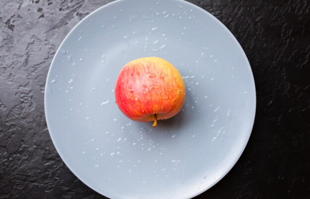 Ein Apfel liegt auf dem grauen Teller. Stilllebenfoto. Schwarzer Hintergrund.