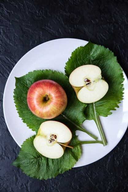 Ein Apfel mit grünen Blättern, die auf dem weißen Teller liegen. Stilllebenfoto. Schwarzer Hintergrund. Obst und Natur.