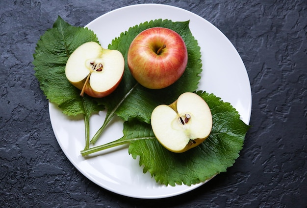 Ein Apfel mit grünen Blättern, die auf dem weißen Teller liegen. Stilllebenfoto. Schwarzer Hintergrund. Obst und Natur.