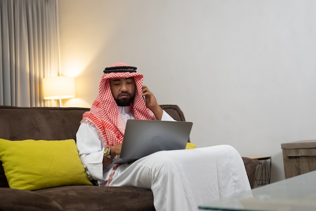 Ein arabischer Geschäftsmann mit Turban telefoniert mit einem Handy und benutzt einen Laptop