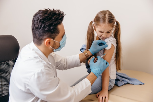 Ein arabischer oder türkischer Arzt gibt einem kleinen Mädchen einen Coronavirus-Impfstoff. Das Mädchen hat Angst. Hochwertiges Foto