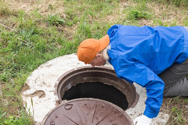 Ein arbeitender Klempner beugte sich über einen Wasserbrunnen, um Rohre und einen Zähler zu inspizieren. Reparatur und Wartung der ländlichen Wasserversorgung