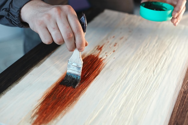 Ein arbeitender Schreiner hält einen Pinsel in der Hand und malt eine Holzoberfläche Eine Farbspur auf einem Holzbrett