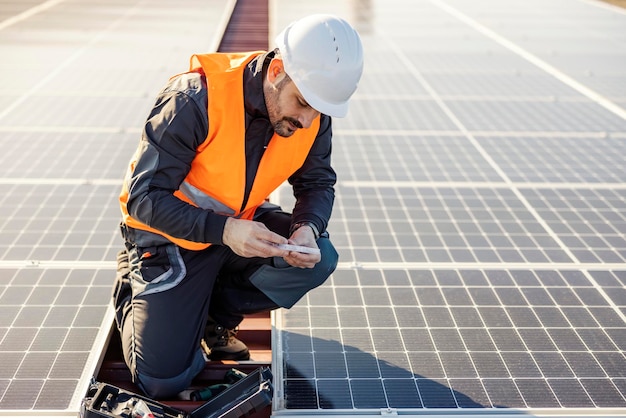 Ein Arbeiter auf dem Dach, der Schrauben aus dem Werkzeugkasten herausholt, um Solarmodule zu installieren