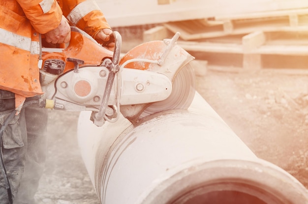 Ein Arbeiter auf der Baustelle schneidet ein Betonabflussrohr mit einer Betonsäge